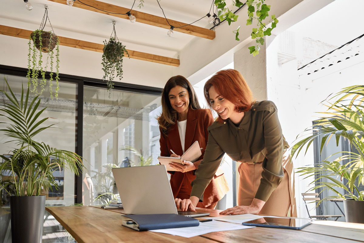 femmes d'affaires heureuses travaillant ensemble au bureau en regardant un ordinateur portable et en écrivant des notes